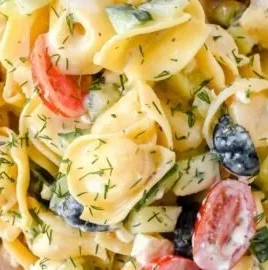 Creamy Greek tortellini salad topped with fresh vegetables and herbs.