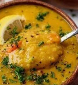 Bowl of lemon lentil soup garnished with fresh herbs and lemon slices.