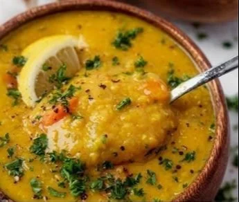 Bowl of lemon lentil soup garnished with fresh herbs and lemon slices.
