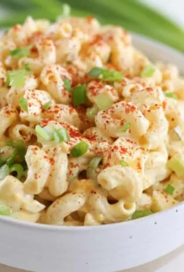 A bowl of Deviled Egg Pasta Salad garnished with herbs and eggs.
