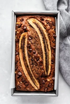 Loaf of healthy banana bread with nuts and banana slices on a wooden table