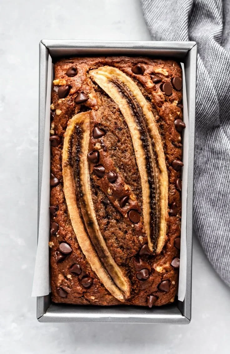 Loaf of healthy banana bread with nuts and banana slices on a wooden table
