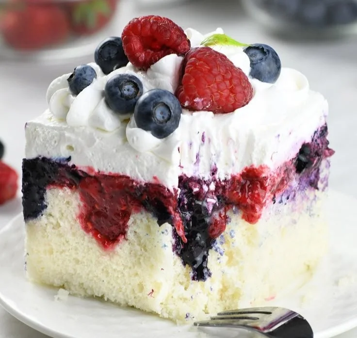 Delicious Summer Berry Poke Cake topped with fresh mixed berries and cream.