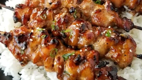 Grilled teriyaki chicken skewers on a serving plate with vegetables