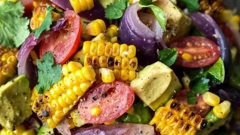 Charred corn avocado salad with roasted red onions in a bowl.