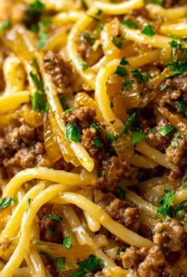 Plate of spaghetti tossed in garlic butter sauce with beef slices and herbs